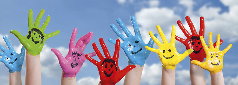 Hände mit Fingerfarbe und Smileys vor blauem Himmel