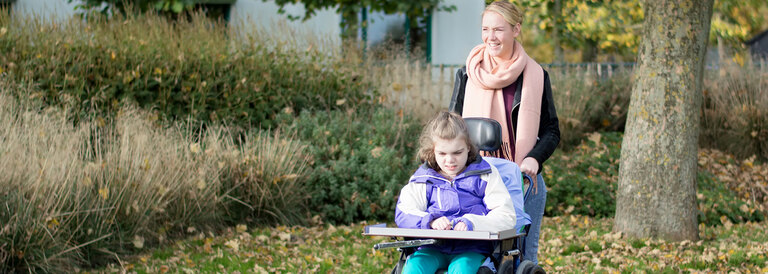 Frau geht mit Kind im Rollstuhl spazieren